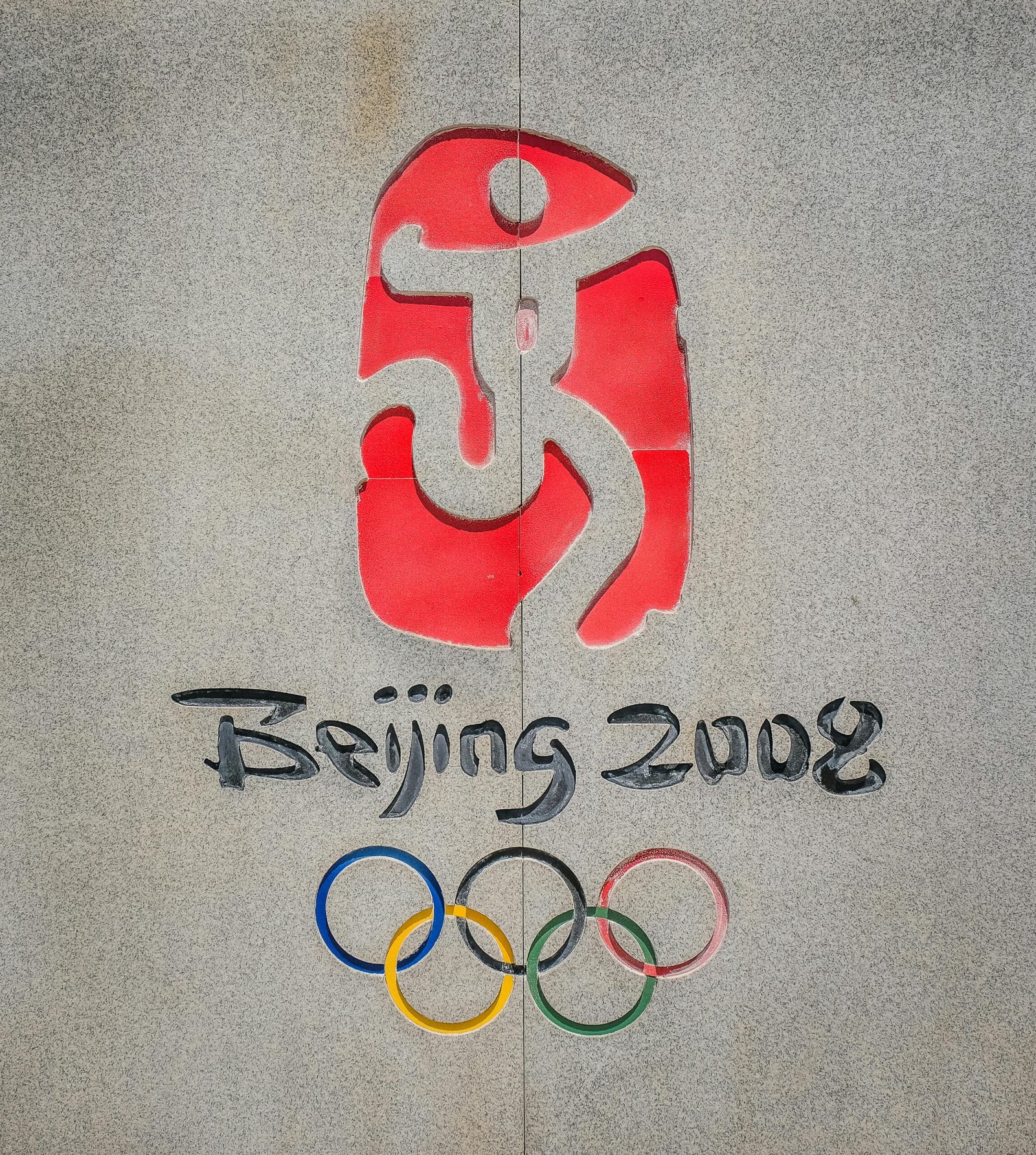 Close-up of the Beijing 2008 Olympic logo and rings on a concrete wall.